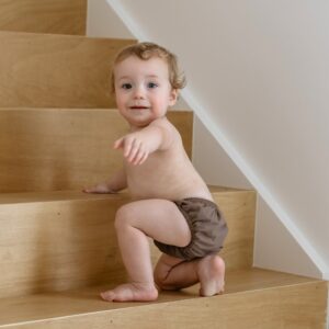 A baby sitting on the stairs in a brown Essentials Range - Lumi Brief Swim Nappy - Tort Colour.