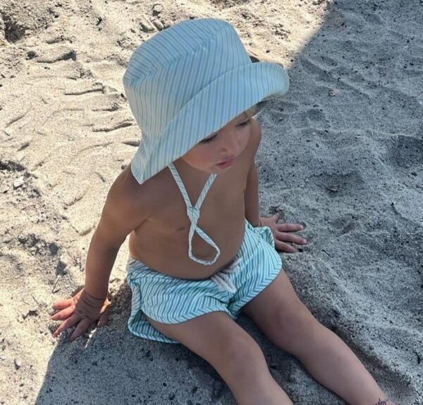 A child sitting on the sand in a Retro Wave By Ina - Vali Bucket Hat.