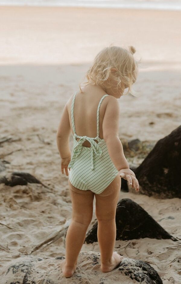 A little girl in a Retro Wave By Ina - Mara One-Piece - Fern Stripe swimsuit standing on the beach.