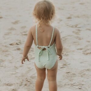 A little girl in a Retro Wave By Ina - Mara One-Piece - Fern Stripe swimsuit standing on the beach.