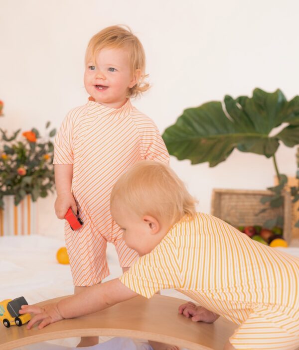Two babies playing with the Retro Wave By Ina - Zimmi Onesie on a wooden table.