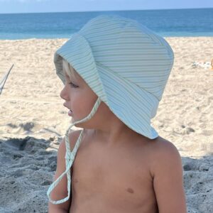 A young boy sitting on the beach wearing a Retro Wave By Ina - Vali Bucket Hat.
