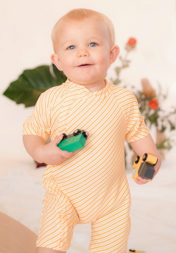 A baby in a yellow striped Retro Wave By Ina - Zimmi Onesie holding a toy car.