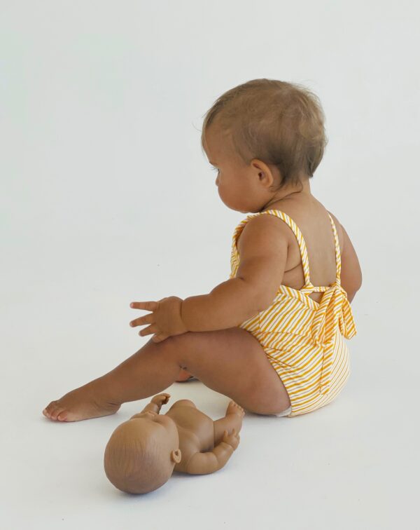 A baby in a Retro Wave By Ina - Mara One-Piece swimsuit next to a doll.