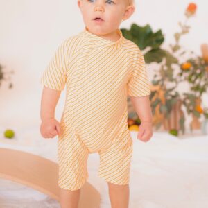 A baby in a Retro Wave By Ina - Zimmi onesie standing on a bed.