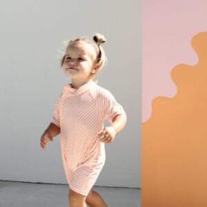 Toddler walking past a Zimmi Onesie - Marigold Stripe backdrop.