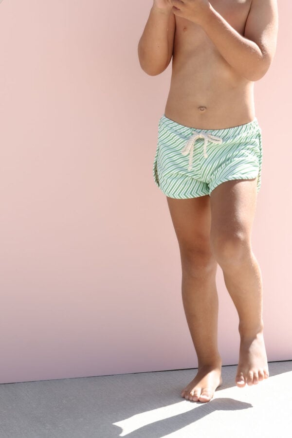 Child in Mesa Trunks - Fern Stripe standing against a pink background.