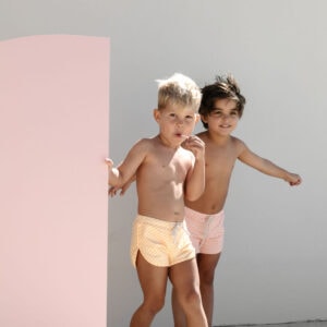 Two young children in swimsuits standing beside a pair of Mesa Trunks - Dandelion Stripe.