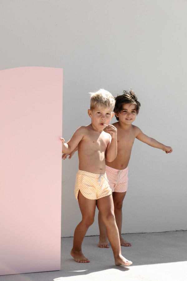 Two young children in swimsuits standing beside a pair of Mesa Trunks - Dandelion Stripe.