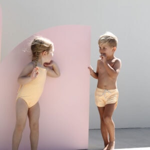 Two children in Mesa Trunks - Dandelion Stripe talking beside pink curved panels.
