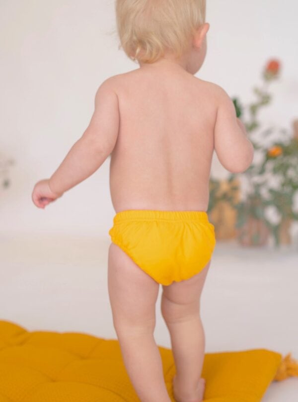 A baby in a Retro Wave By Ina - Lumi Brief Swim Nappy standing on a rug.