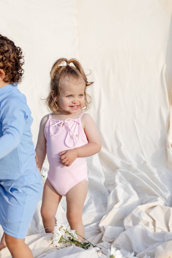 Two children in WS - Golden Meadows Collection - Aurelia One-Piece swimsuits playing on a white sheet.