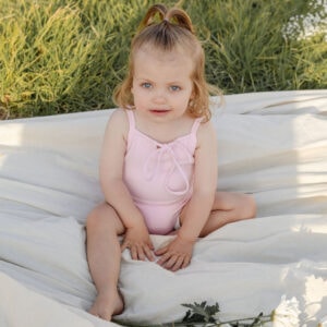 A little girl sitting on a blanket in a field wearing the WS - Golden Meadows Collection - Aurelia One-Piece.