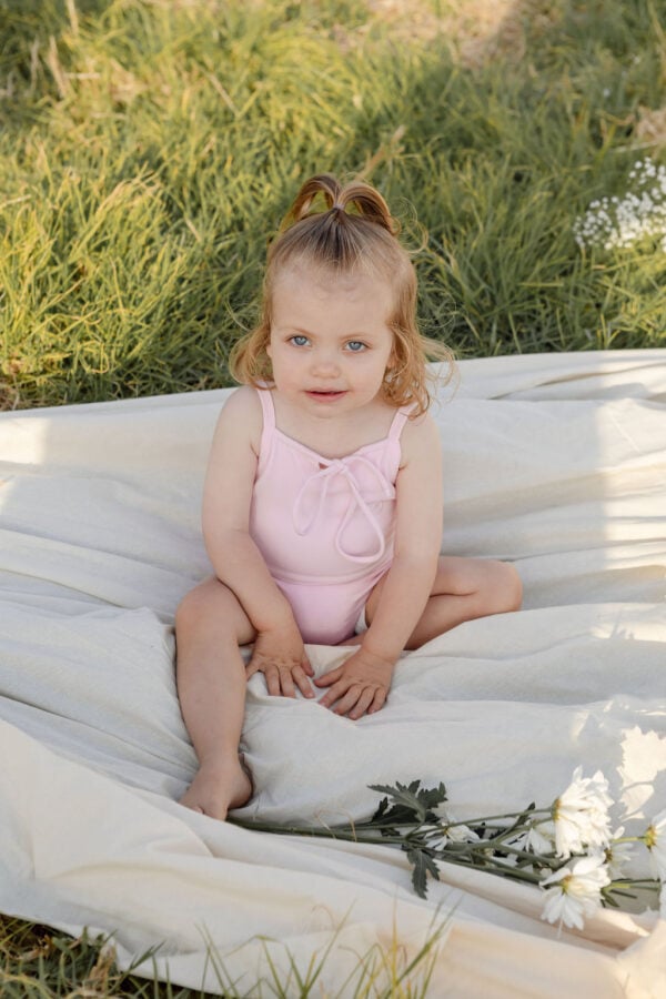 A little girl sitting on a blanket in a field wearing the WS - Golden Meadows Collection - Aurelia One-Piece.