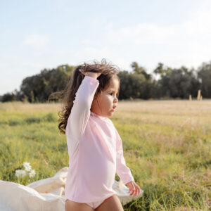 A little girl standing on a blanket in a field, wearing the WS - Golden Meadows Collection - Nella Rash Shirt.