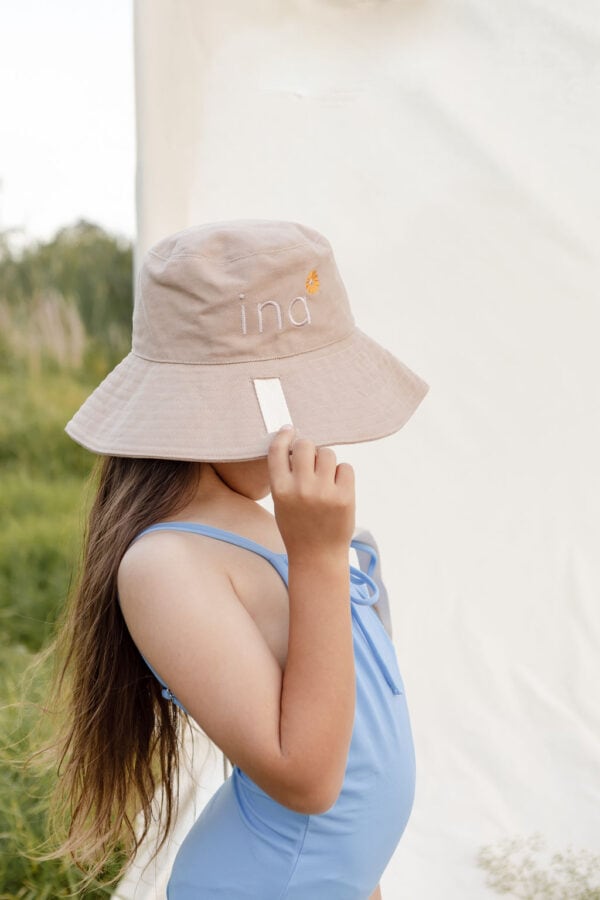 A little girl in a blue swimsuit wearing the WS - Golden Meadows Collection - Golden Sun Bucket Hat.