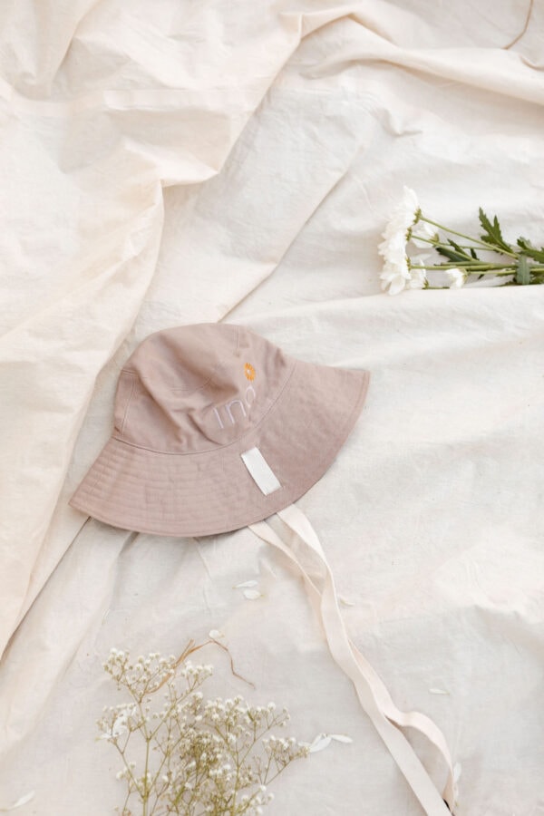 The WS - Golden Meadows Collection - Golden Sun Bucket Hat, laying on a bed with flowers on it.