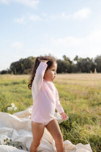 Young child standing in a field with a thoughtful pose.