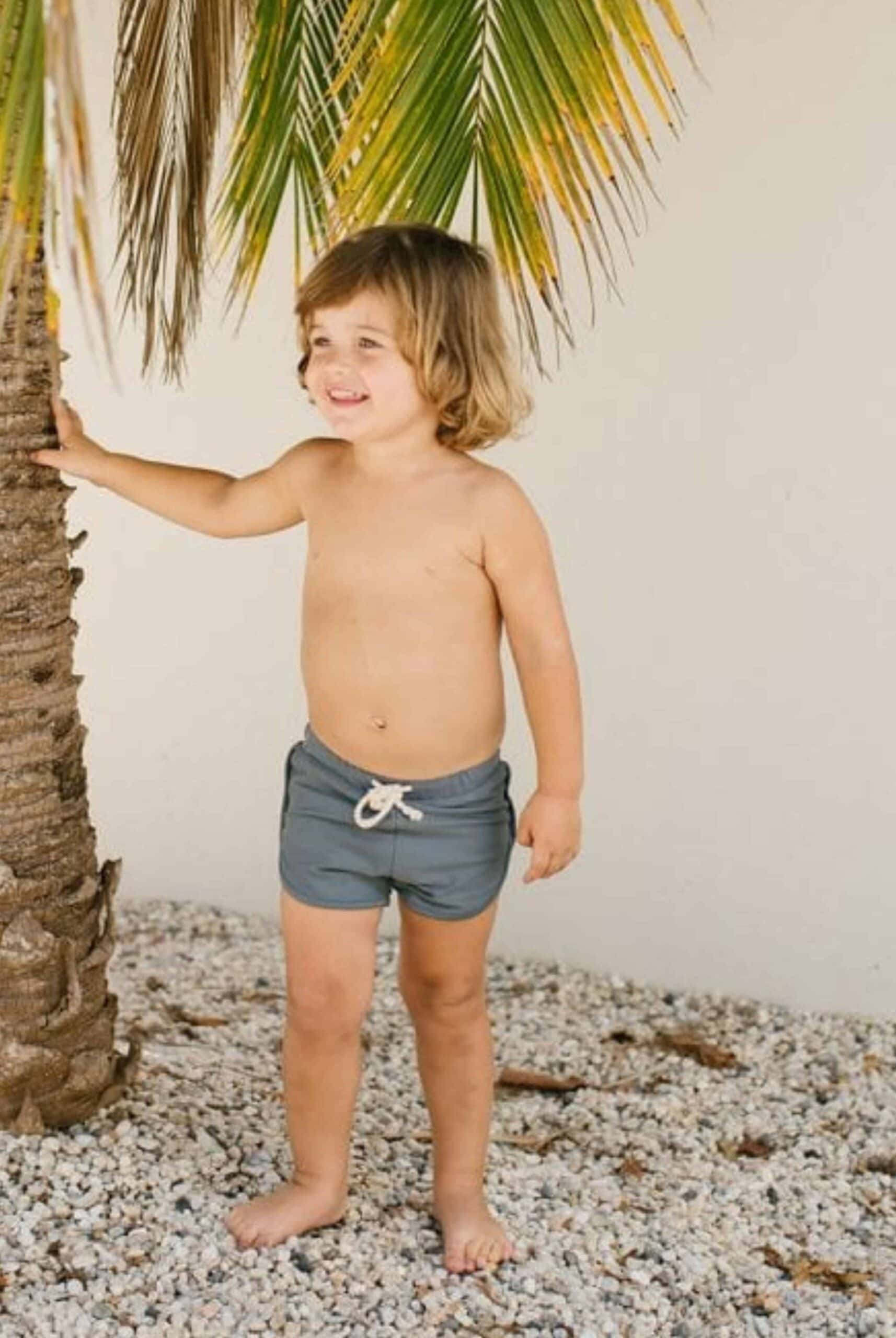 A young boy is standing next to a palm tree.