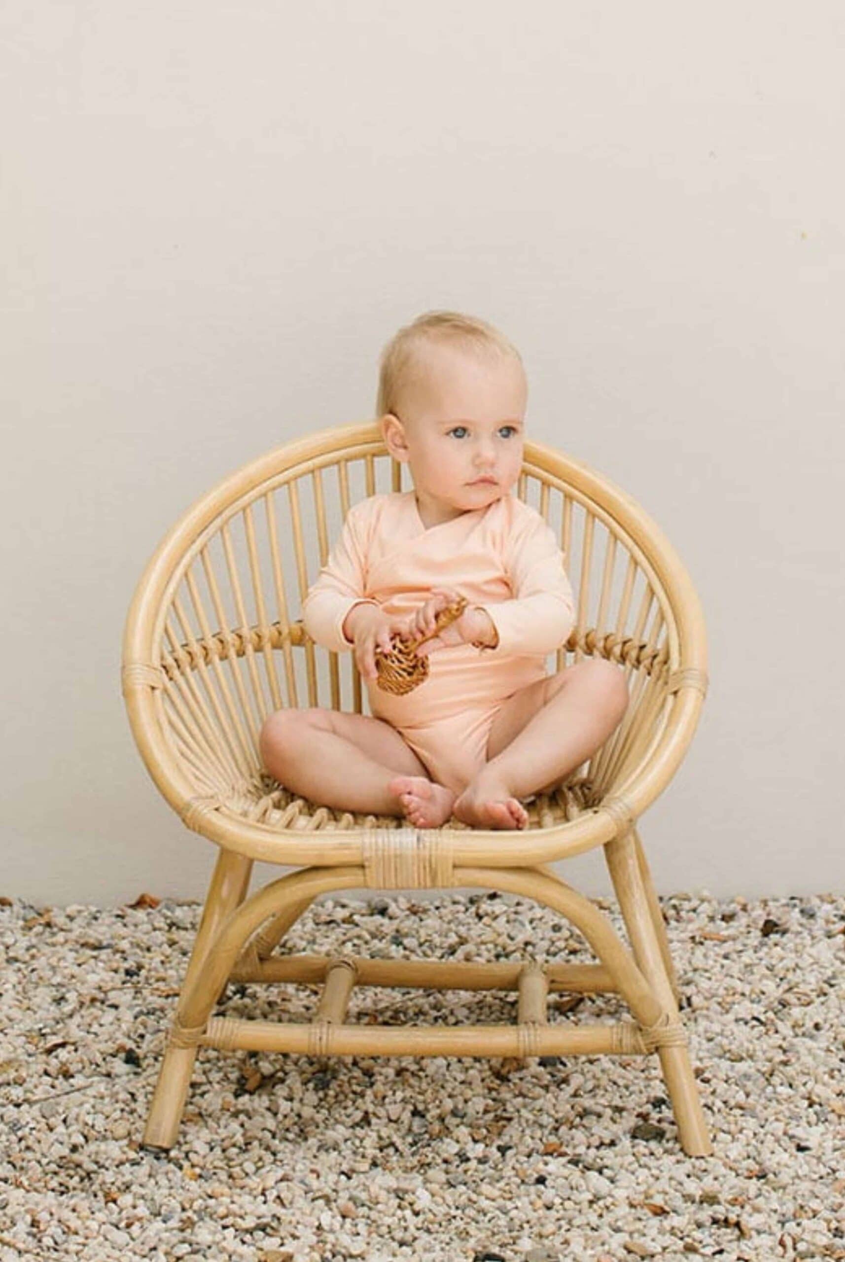 A baby sitting in a rattan chair.