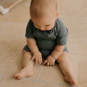 A baby is sitting on a Mineral Onesie - Zimmi tile floor.