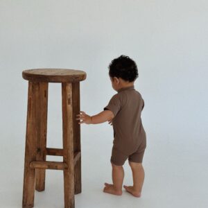 A baby standing next to a Zimmi Onesie - Tort stool.