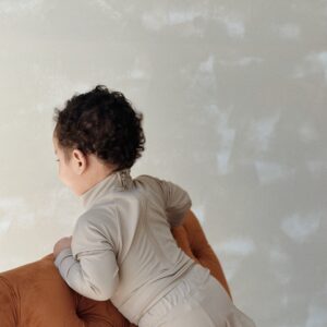 A baby sitting on an Essentials Range - June One-Piece - Sand Colour couch.