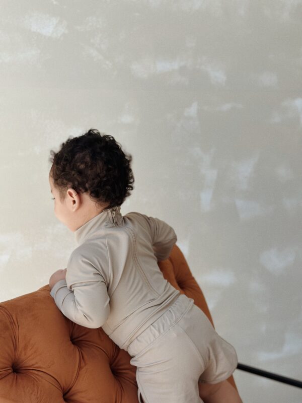 A baby sitting on an Essentials Range - June One-Piece - Sand Colour couch.