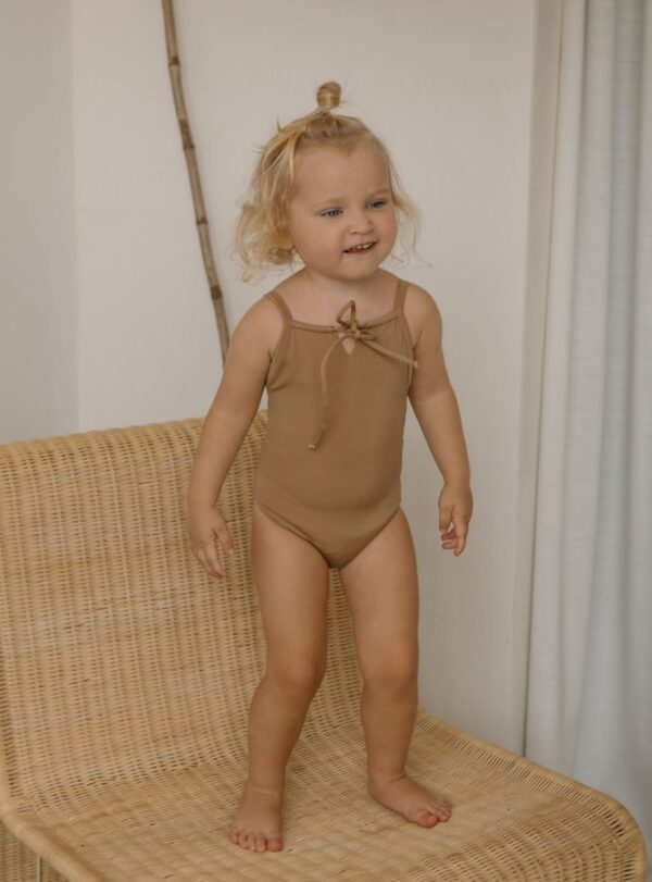 Toddler standing on a wicker chair in a Aurelia One-Piece - Warm Pecan swimsuit.