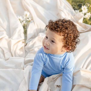 Toddler with curly hair playing on a Nella Rash Shirt - Powder Sky blanket outdoors.