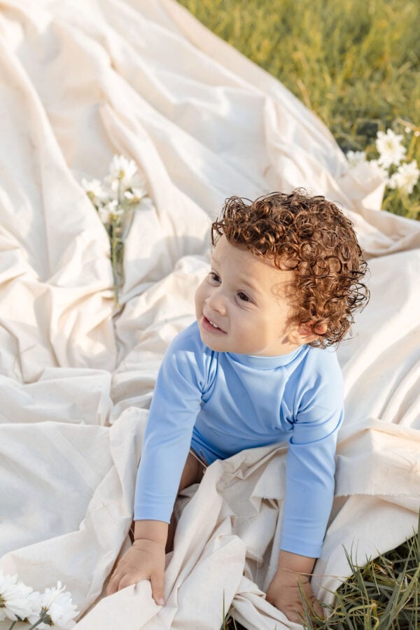 Toddler with curly hair playing on a Nella Rash Shirt - Powder Sky blanket outdoors.