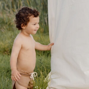 Toddler with curly hair standing next to a Mesa Trunks - Warm Pecan outdoors.
