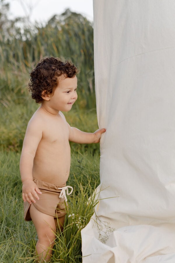 Toddler with curly hair standing next to a Mesa Trunks - Warm Pecan outdoors.