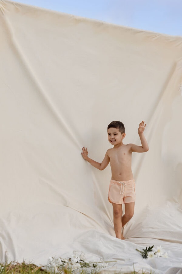 A young boy in Amias Trunks - Peach Blossom standing against a neutral backdrop with a playful pose.