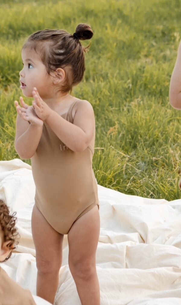 Toddler standing on a Mara One-Piece - Warm Pecan outdoors with hands together in a clapping gesture.