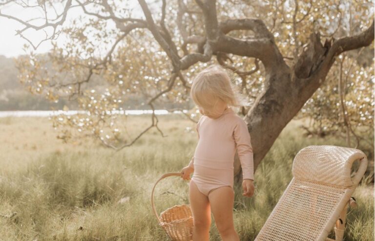 Young child holding a basket near a tree in a sunny field.